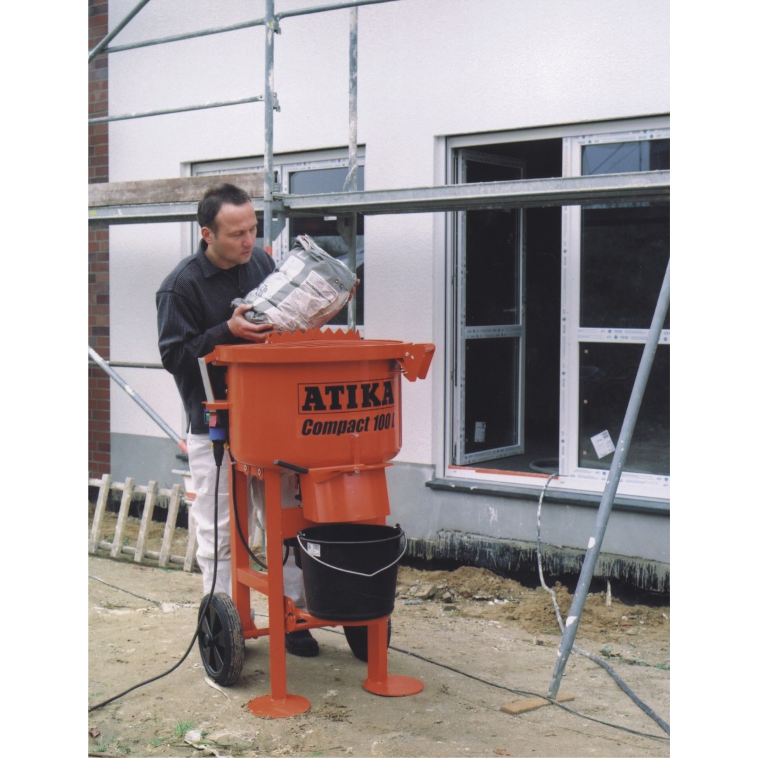 Atika Compact 100 pan mixer in use on site with a plasterer pouring a bagged mix into the mixing drum.